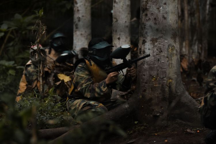 Paintballers getting cover behind a tree