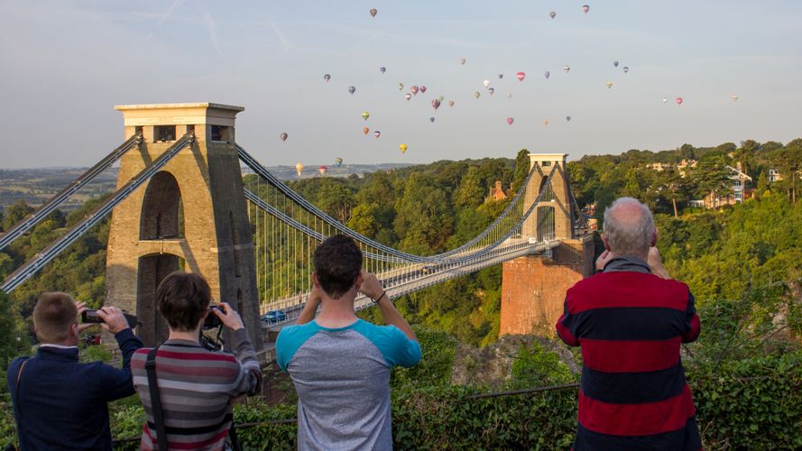 A grandparent with children taking pictures of hot air balloons over Clifton Suspension Bridge