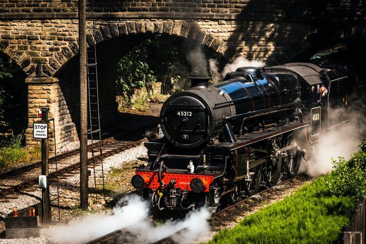 Black and red steam train passing under a bridge 