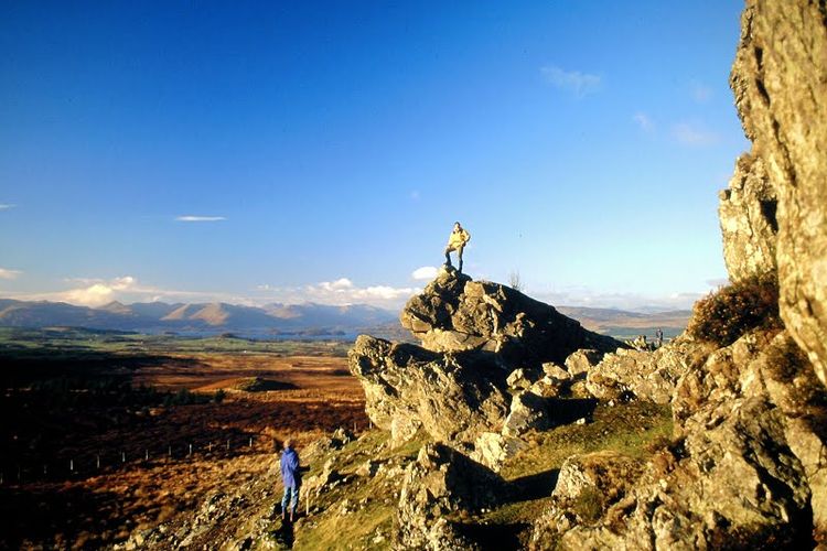 A hiker posing on top of a rock in the Whangie, Scotland