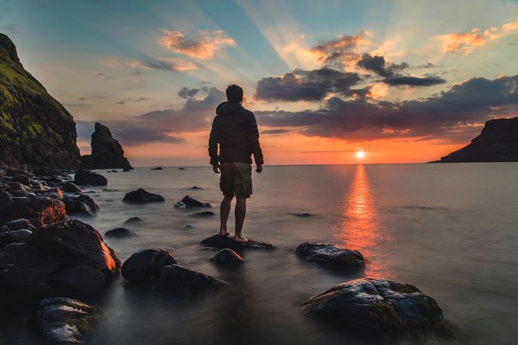 Man standing on stone in the sea looking at the sunset